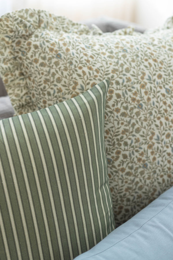 Green and cream striped pillow in foreground with floral patterned pillows behind it on bed.