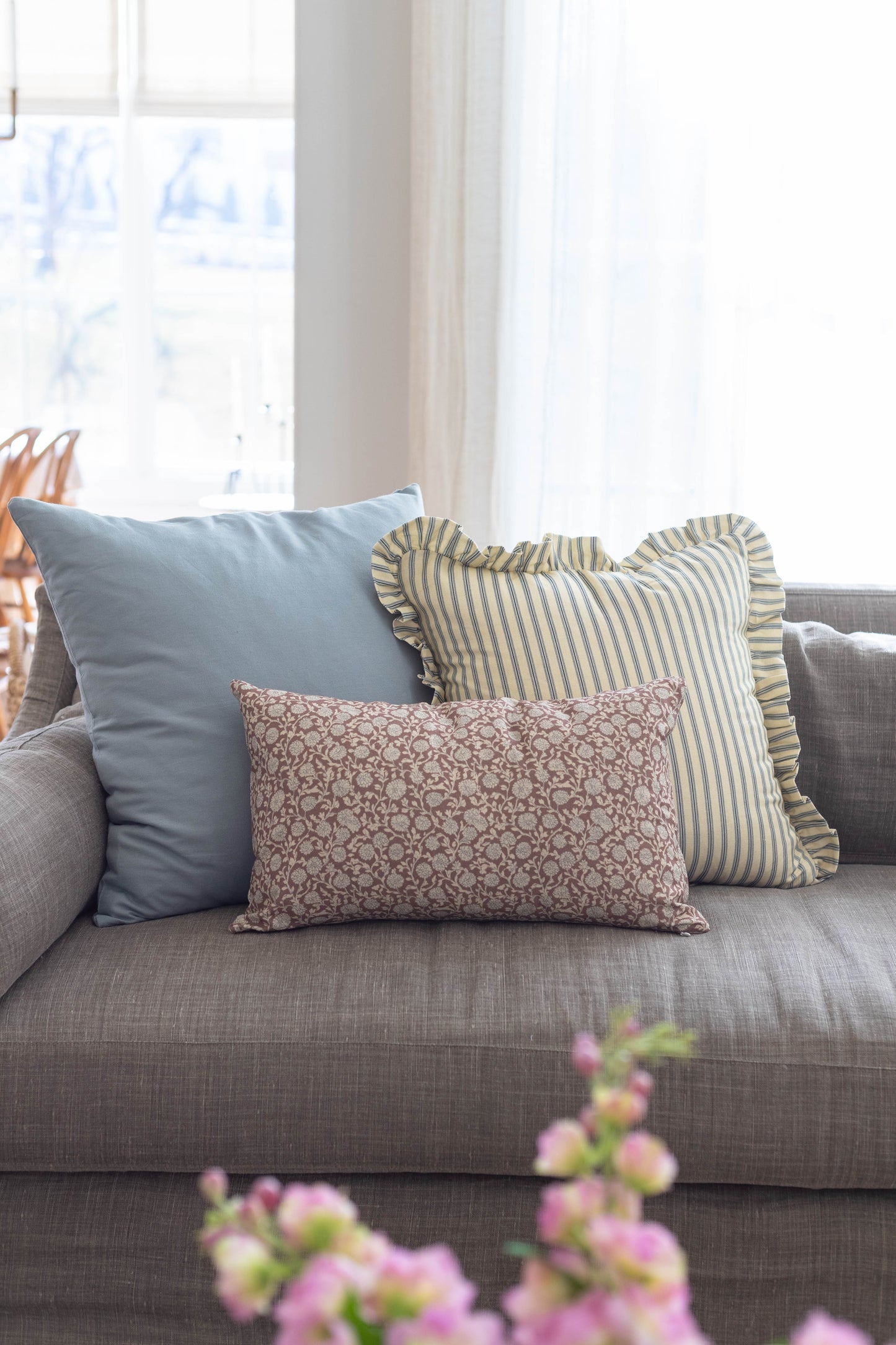 Three decorative pillows on gray sofa: solid blue pillow, yellow striped pillow with ruffled edges, and taupe patterned pillo