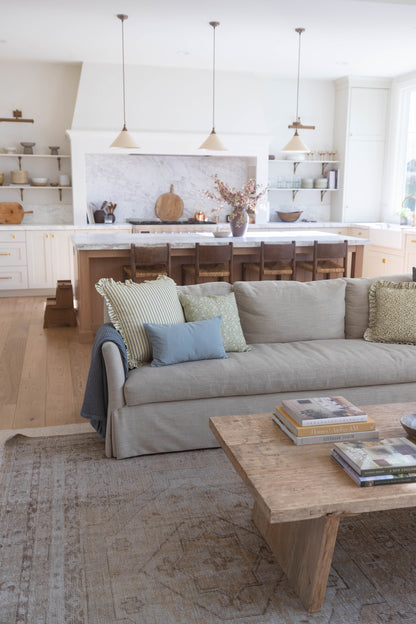 Beige linen sofa with ruffled skirt and decorative pillows in open kitchen and living room setting.