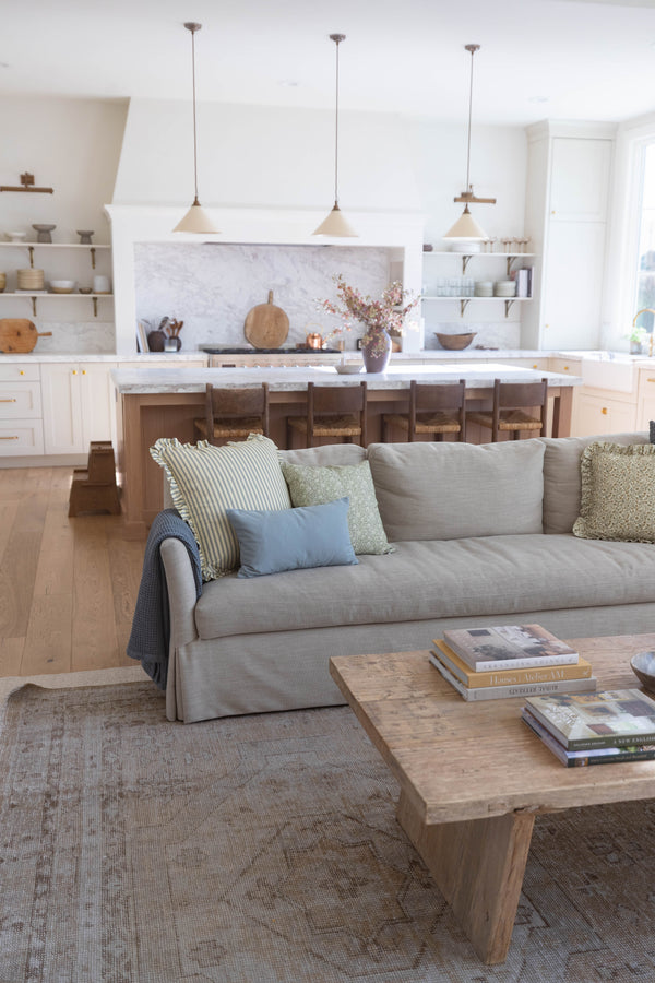 Beige linen sofa with ruffled skirt and decorative pillows in open kitchen and living room setting.