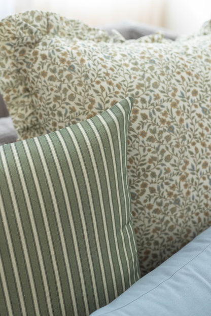 Decorative pillows with floral and striped patterns in sage green, tan, and cream tones with ruffled edges.
