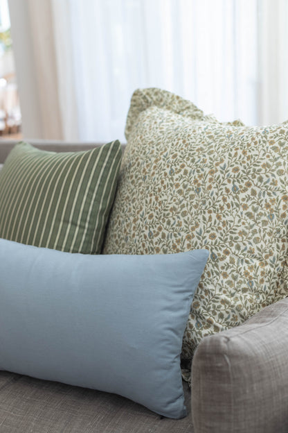 Decorative pillows in sage green striped, cream floral, and blue solid patterns arranged on a sofa.