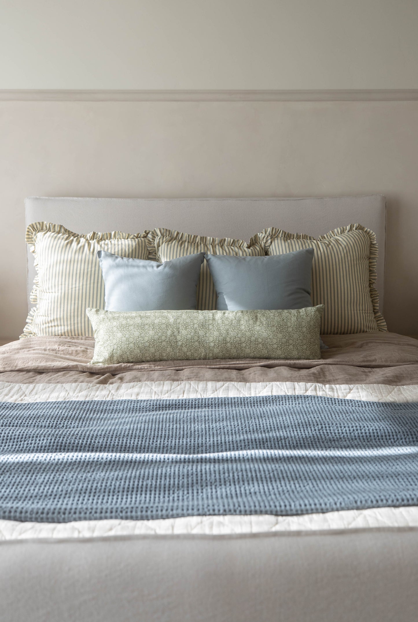Striped Ellis Ruffle pillow with ruffled edges displayed on bed among blue and green patterned pillows.