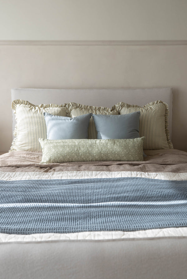 Striped Ellis Ruffle pillow with ruffled edges displayed on bed among blue and green patterned pillows.