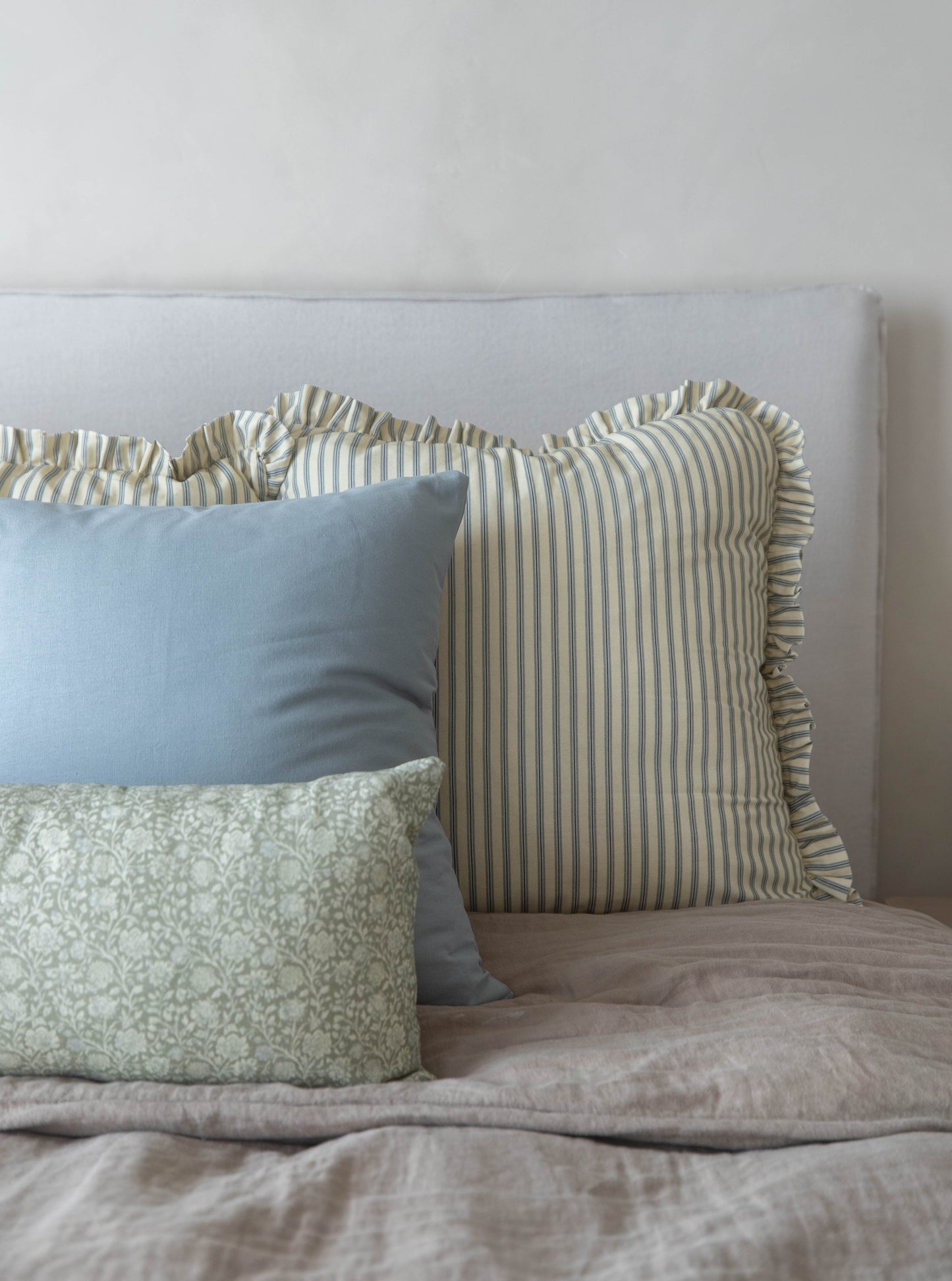 Light blue, green patterned, and tan striped throw pillows with ruffled edges arranged on a bed.