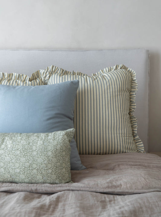 Light blue, green patterned, and tan striped throw pillows with ruffled edges arranged on a bed.