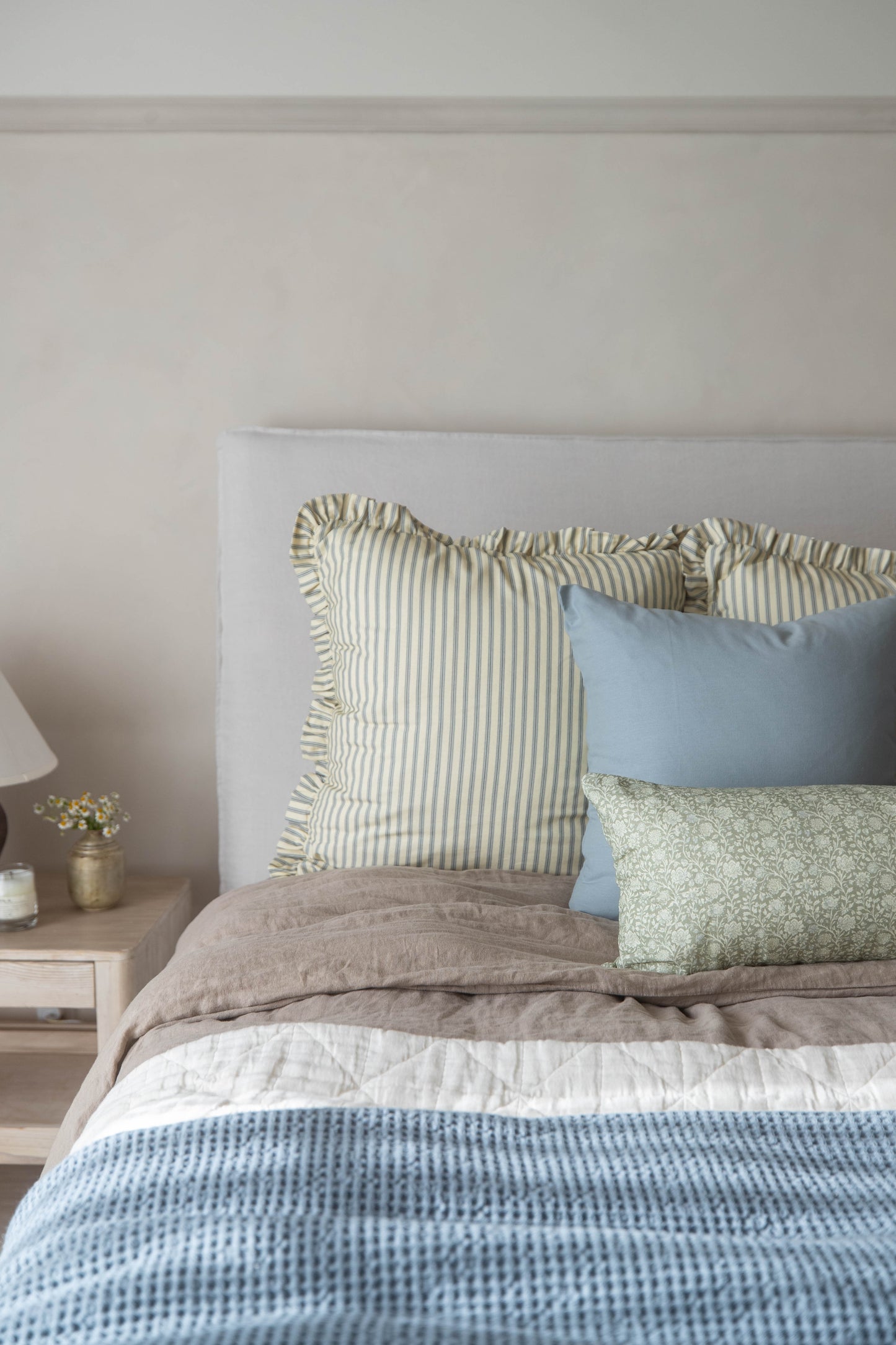 Cream striped pillow with ruffled edges displayed on a bed with blue and green pillows.