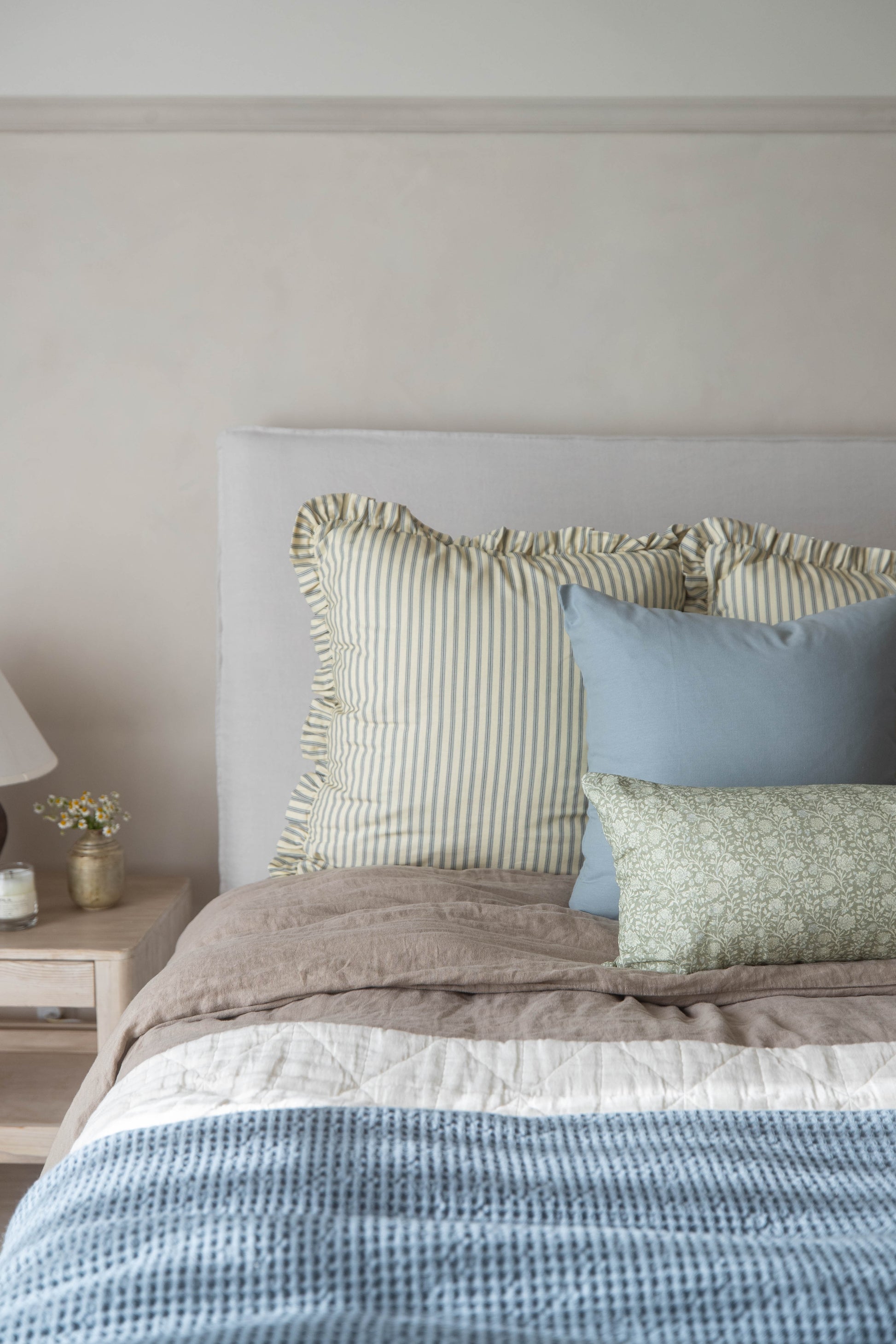 Cream striped pillow with ruffled edges displayed on a bed with blue and green pillows.