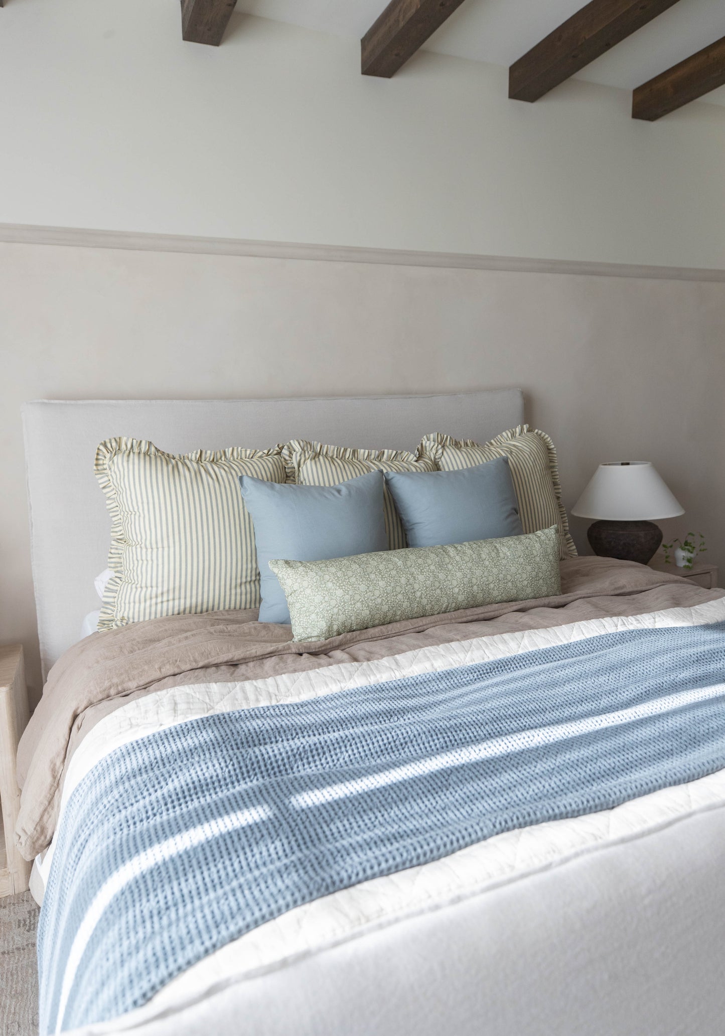 Bed with white upholstered headboard, layered with striped and solid blue pillows and green rectangular pillow, blue and whit