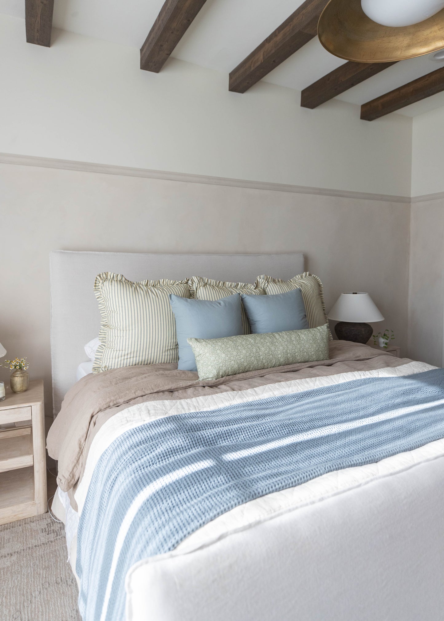 Bed with white upholstered headboard, striped and blue pillows, blue and white patterned bedding, and beige throw blanket in 