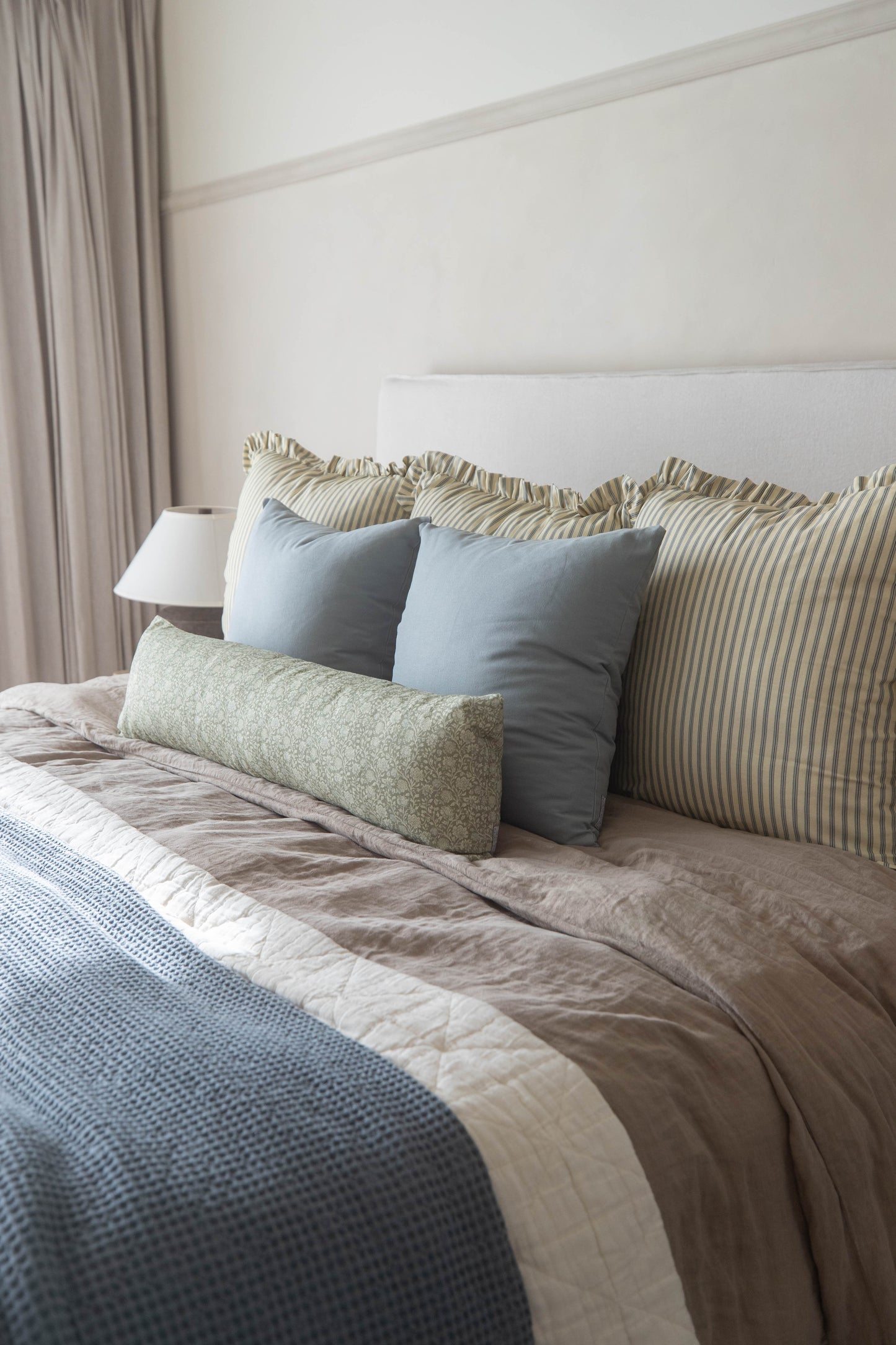 Striped and solid decorative pillows with ruffled edges arranged on a bed with blue and neutral bedding.