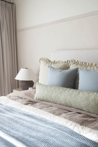 Striped ruffle pillows in cream and tan on a bed with blue and green bedding.