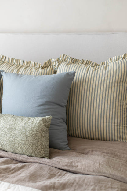 Striped and patterned throw pillows with ruffled edges arranged on a bed with neutral bedding.
