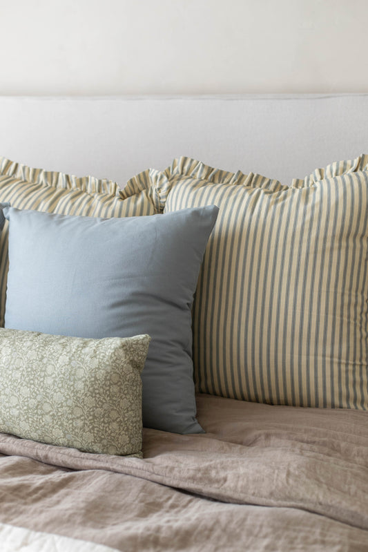 Striped and patterned throw pillows with ruffled edges arranged on a bed with neutral bedding.