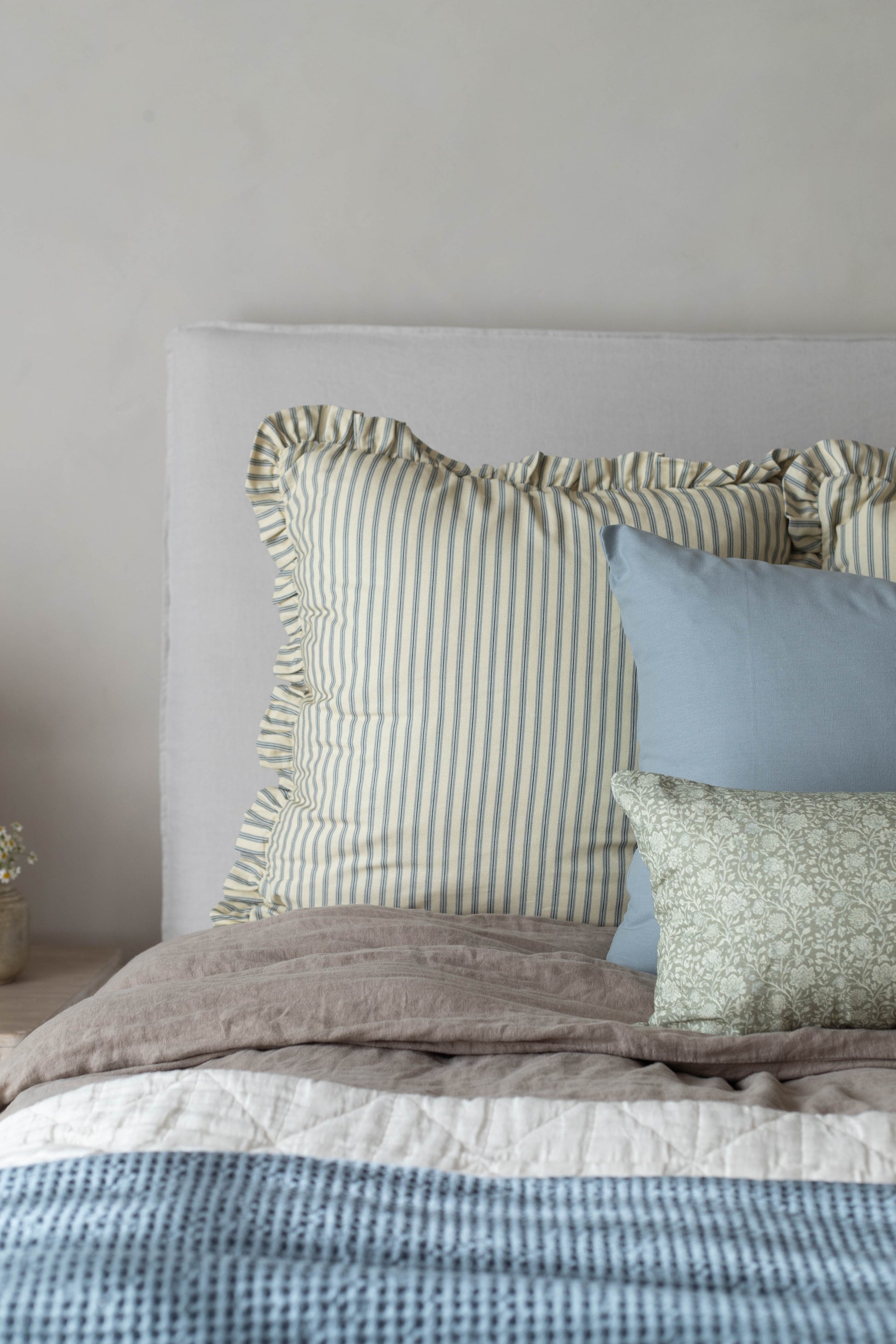 Green and white striped pillow with ruffled edges displayed on a bed with blue and patterned pillows.