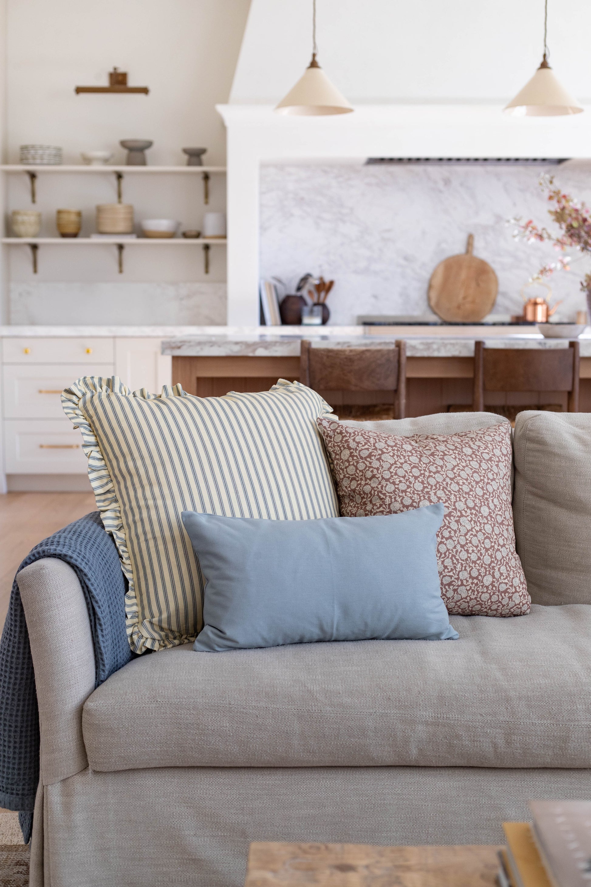 Light blue rectangular pillow on beige sofa with striped and patterned pillows in modern kitchen setting.