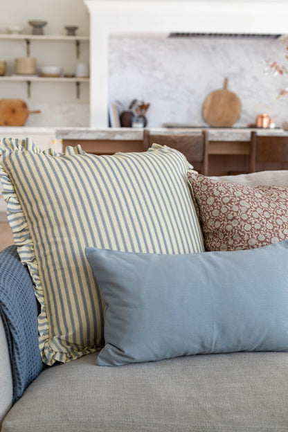 Striped cream and blue pillow with ruffled edges displayed on a beige sofa with patterned and solid pillows.