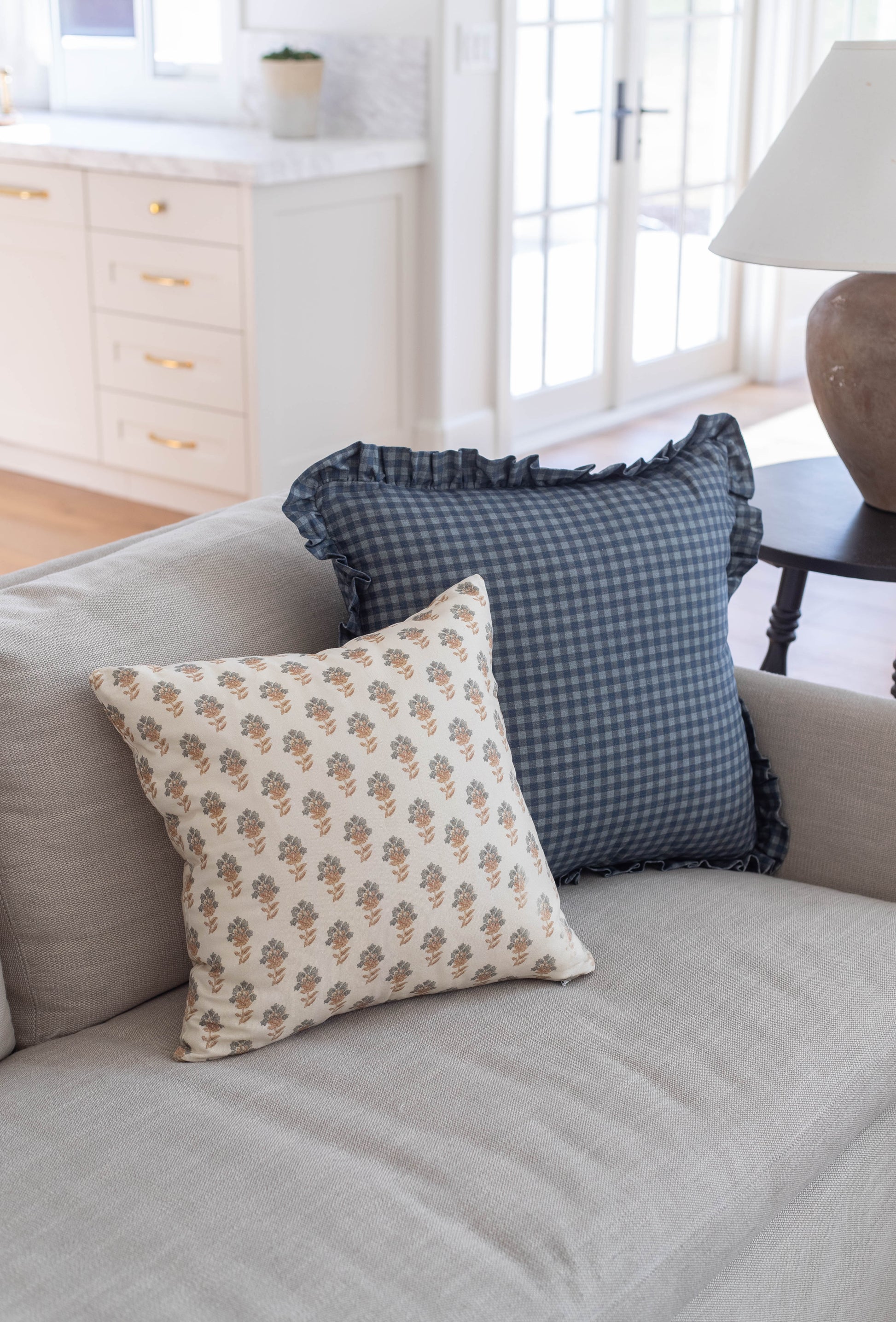 Navy gingham pillow with ruffle edge detail displayed on a beige sofa.