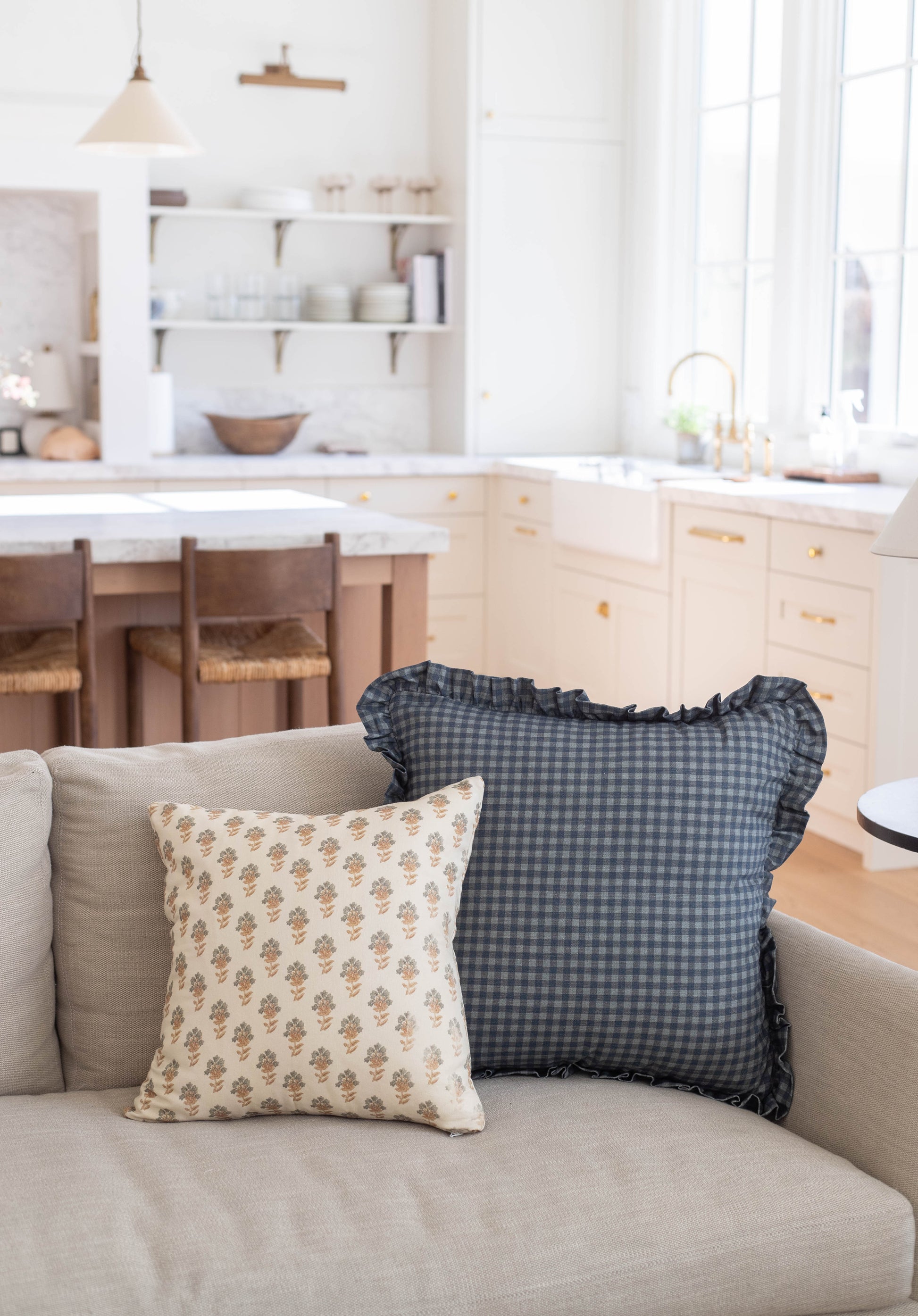 Navy gingham pillow with ruffled edges displayed on a beige sofa.