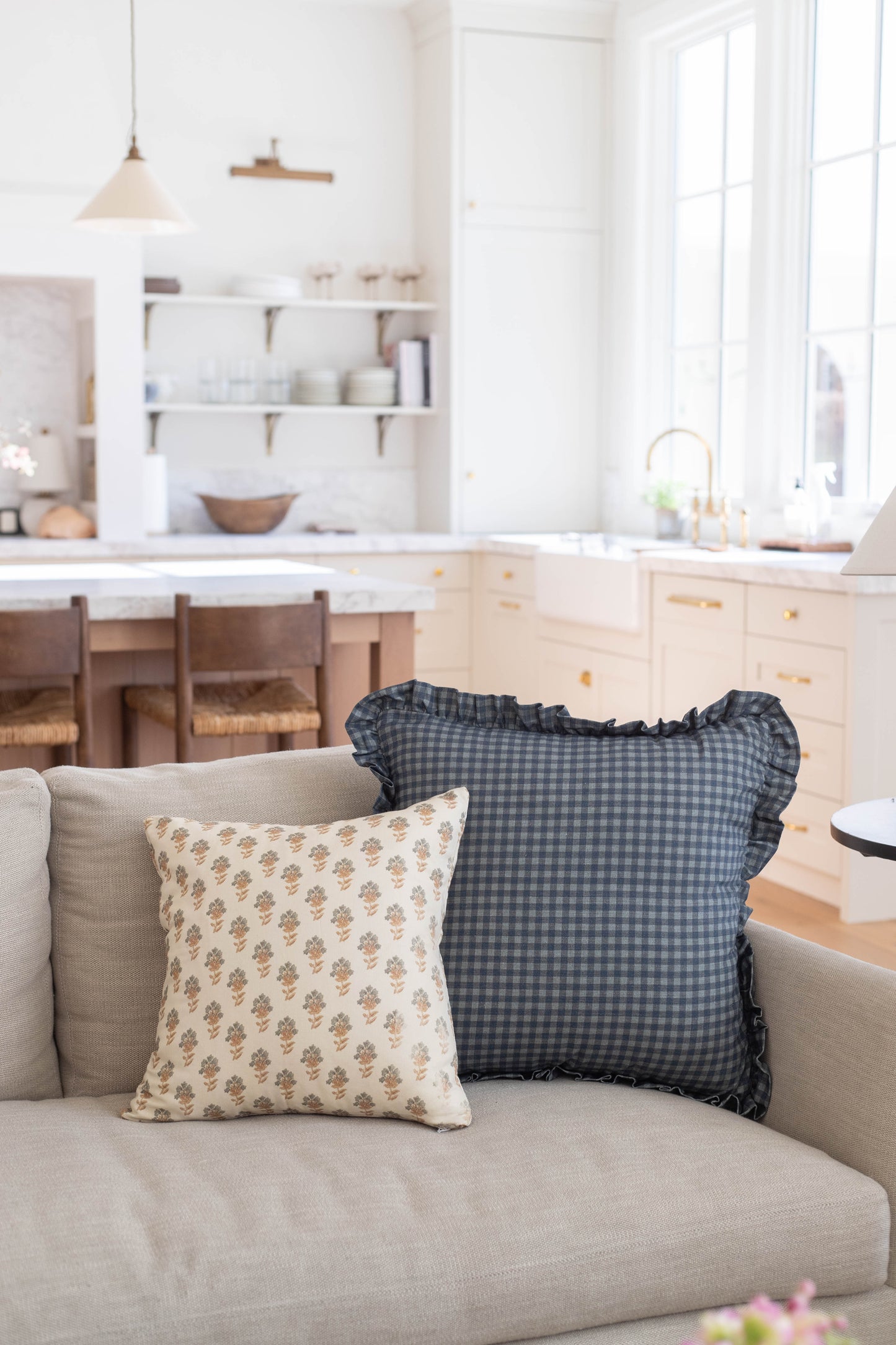 Two decorative pillows on a cream sofa: one with tan floral print and one with navy gingham pattern and ruffled edges.