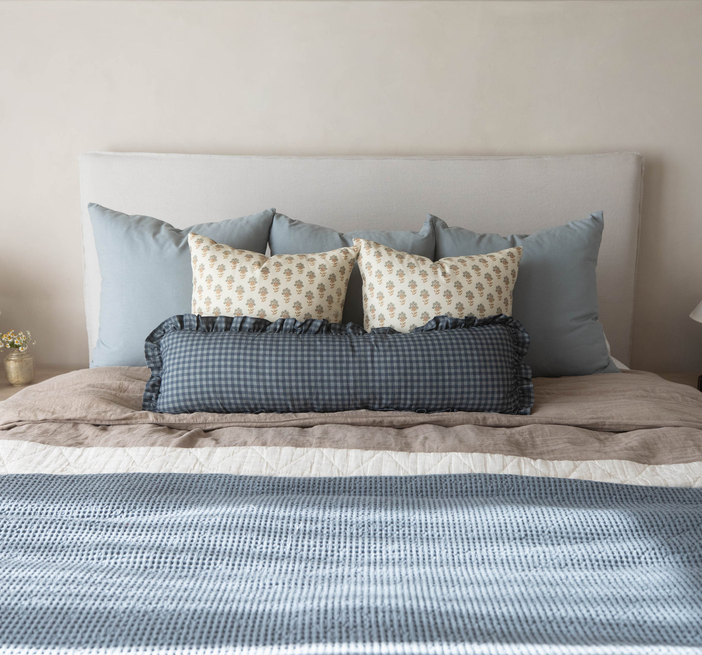 Navy gingham lumbar pillow with ruffled edges displayed on a bed with coordinating pillows.