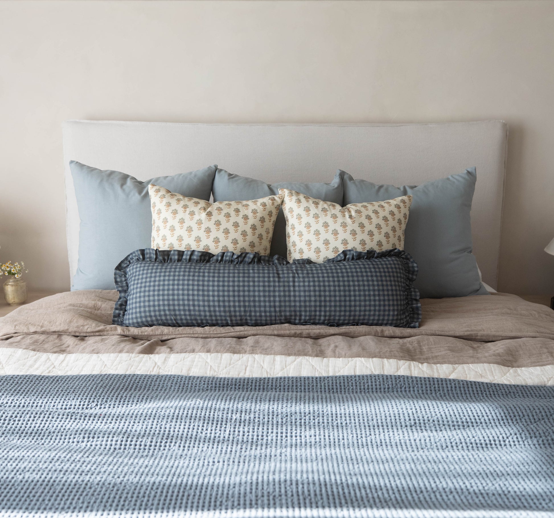 Navy gingham lumbar pillow with ruffled edges displayed on a bed with coordinating pillows.