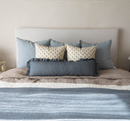 Navy gingham lumbar pillow with ruffled edges displayed on a bed with coordinating pillows.