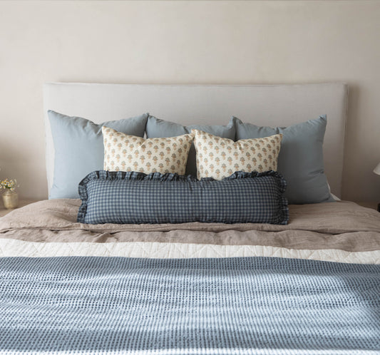 Navy gingham lumbar pillow with ruffled edges displayed on a bed with coordinating pillows.
