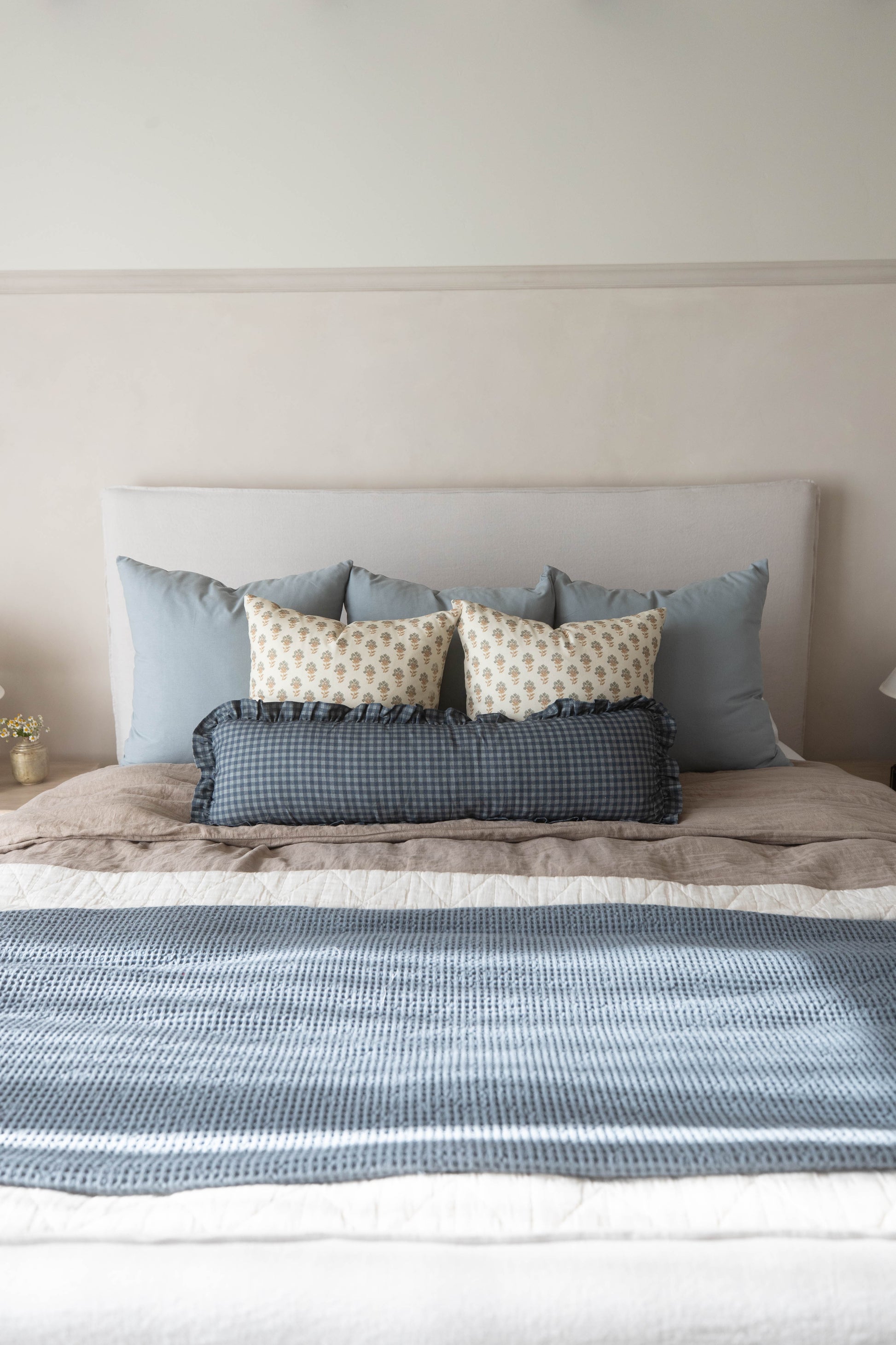 Navy gingham lumbar pillow with ruffled edges displayed on a bed with blue and cream pillows.