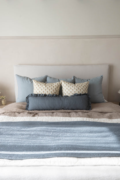 Navy gingham lumbar pillow with ruffled edges displayed on a bed with blue and cream pillows.