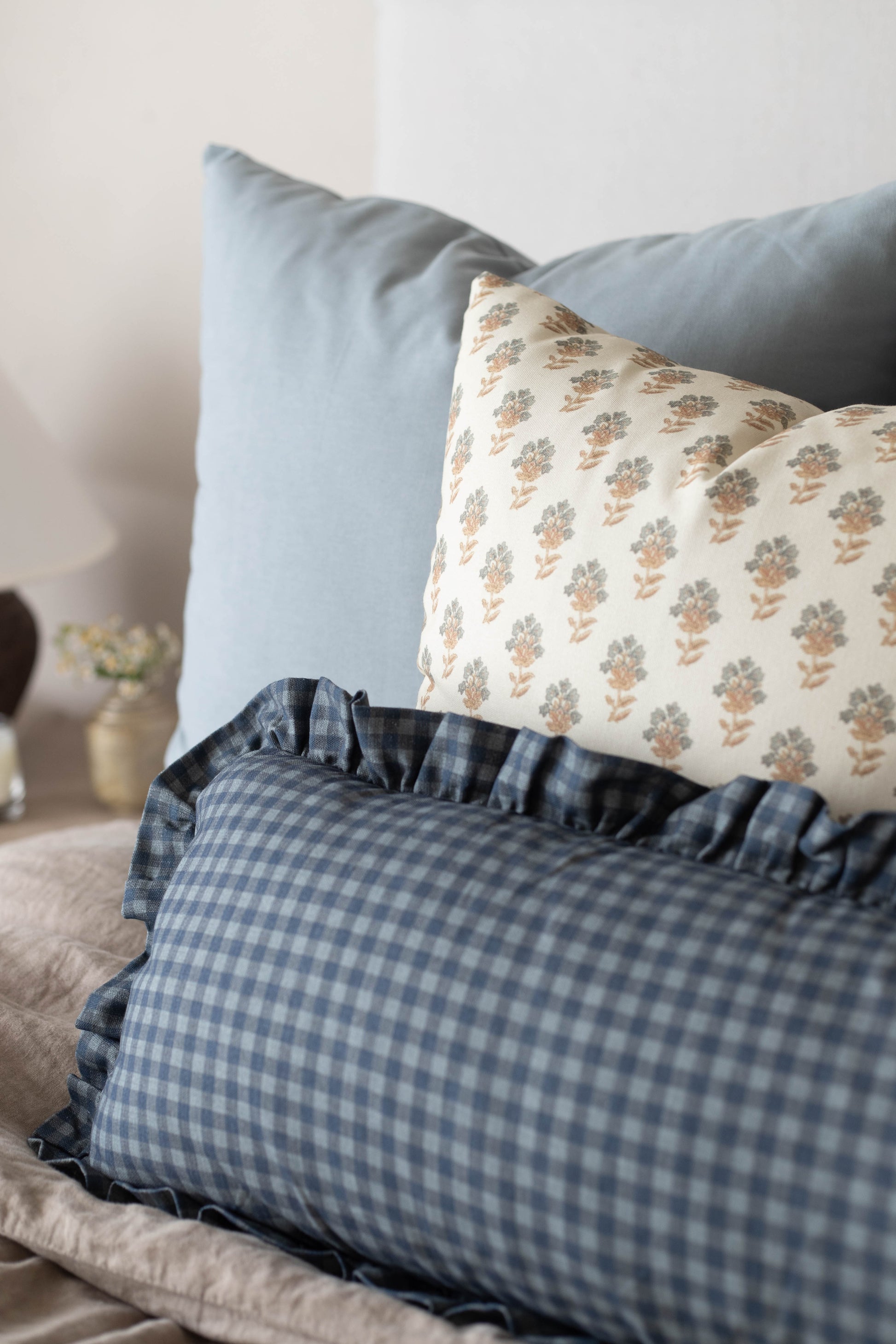 Navy gingham pillow with ruffled edges displayed on a bed with decorative pillows.