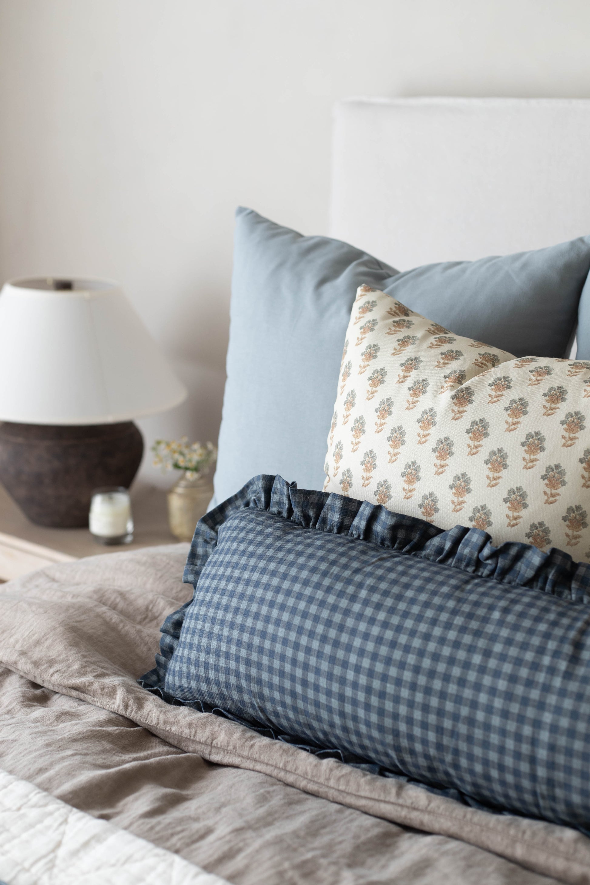 Decorative pillow with blue gingham pattern and ruffled edges displayed on bed with floral and solid pillows.