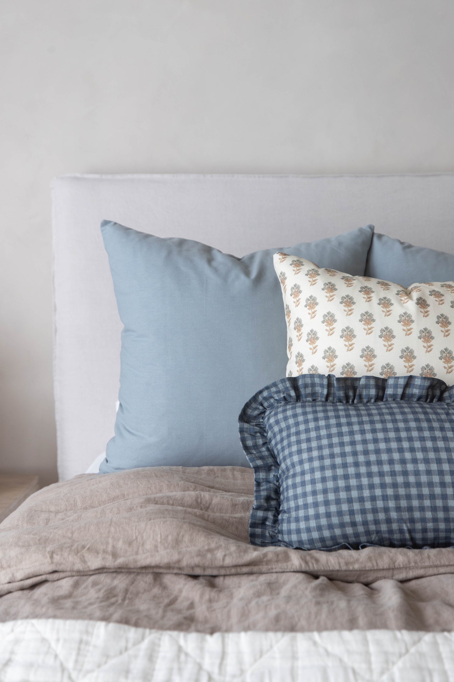 Navy gingham pillow with ruffled edges displayed on a bed with blue and patterned pillows.