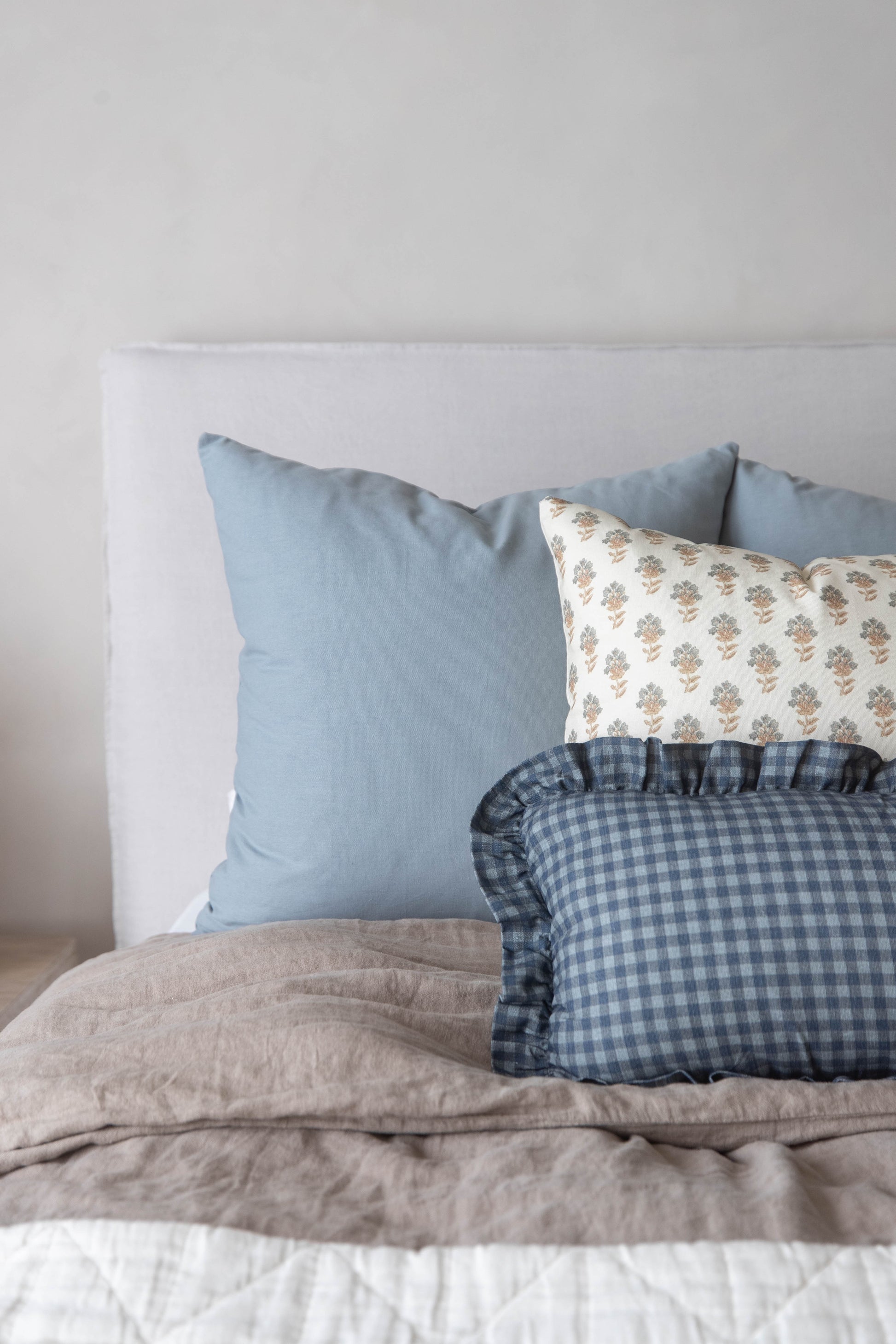Navy gingham pillow with ruffled edges displayed on a bed with blue and patterned pillows.