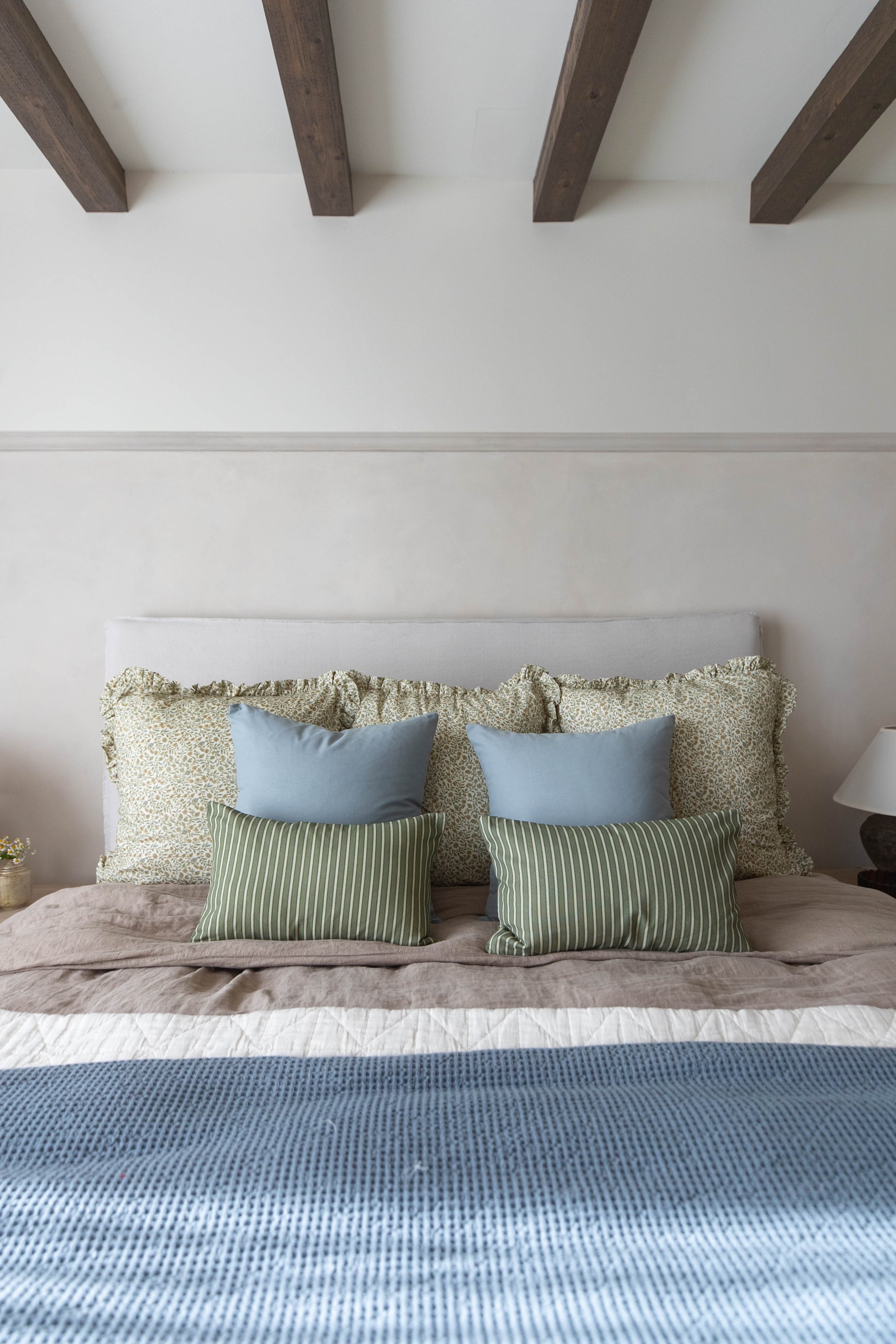 Bed with light gray upholstered headboard, layered with green and blue throw pillows and a blue waffle-weave bedcover.