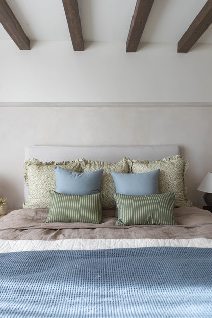 Bed with light gray upholstered headboard, layered with green and blue throw pillows and a blue waffle-weave bedcover.