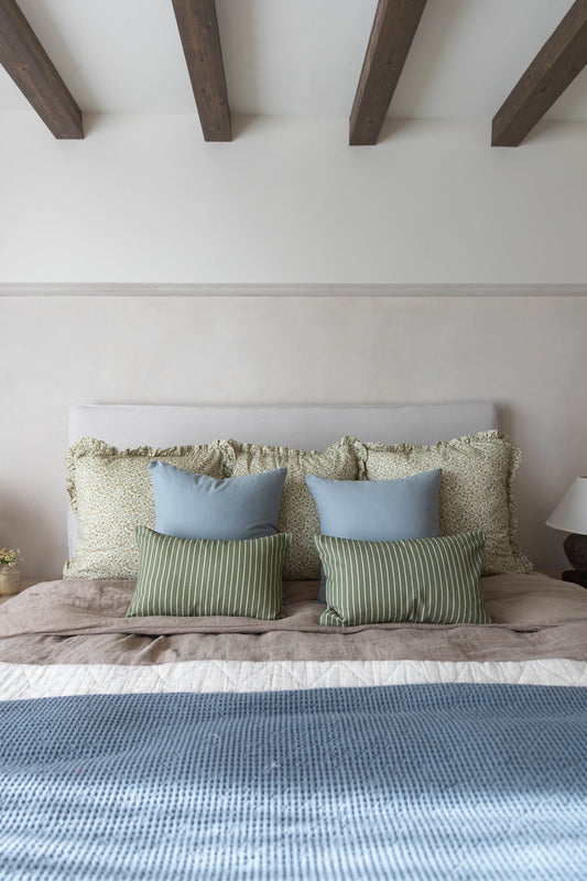 Bed with light gray upholstered headboard, layered with green and blue throw pillows and a blue waffle-weave bedcover.