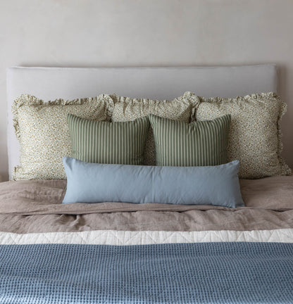 Bed arrangement with ruffled cream floral pillows, green striped pillows, and blue rectangular pillow against white headboard