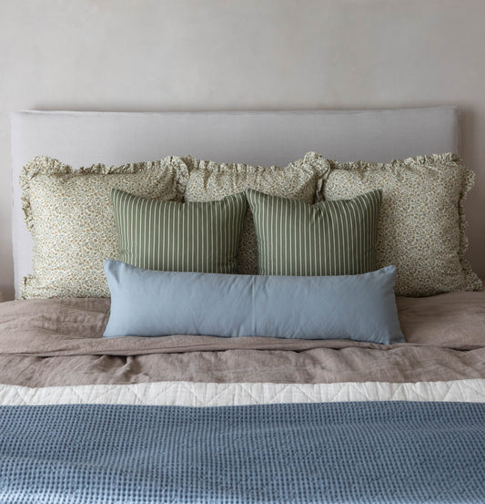 Bed arrangement with ruffled cream floral pillows, green striped pillows, and blue rectangular pillow against white headboard