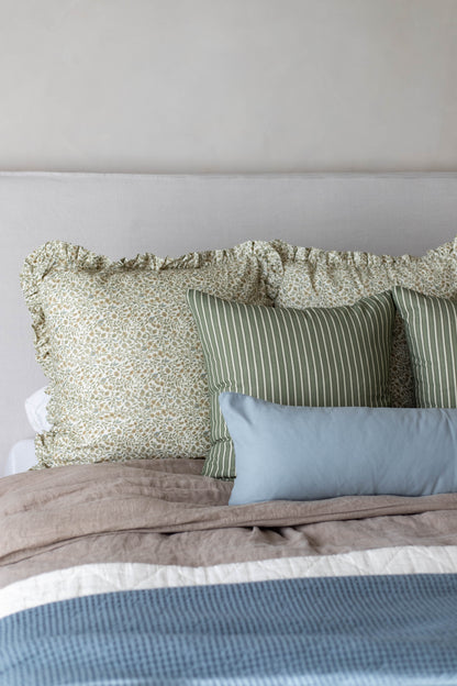 Bed with layered pillows in green floral and striped patterns, light blue rectangular pillow, and tan and white bedding.
