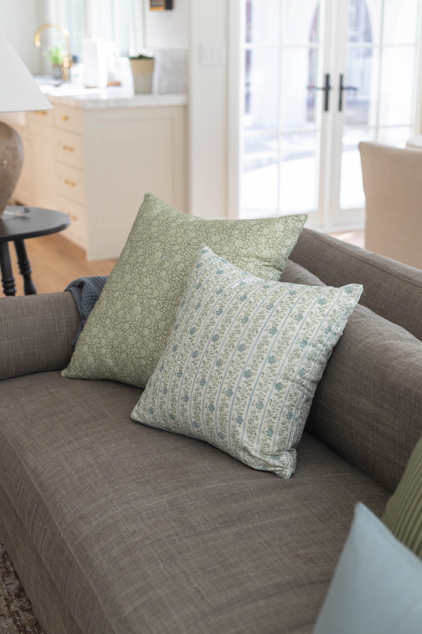 Green and cream patterned throw pillows arranged on a gray upholstered sofa in a bright living room.