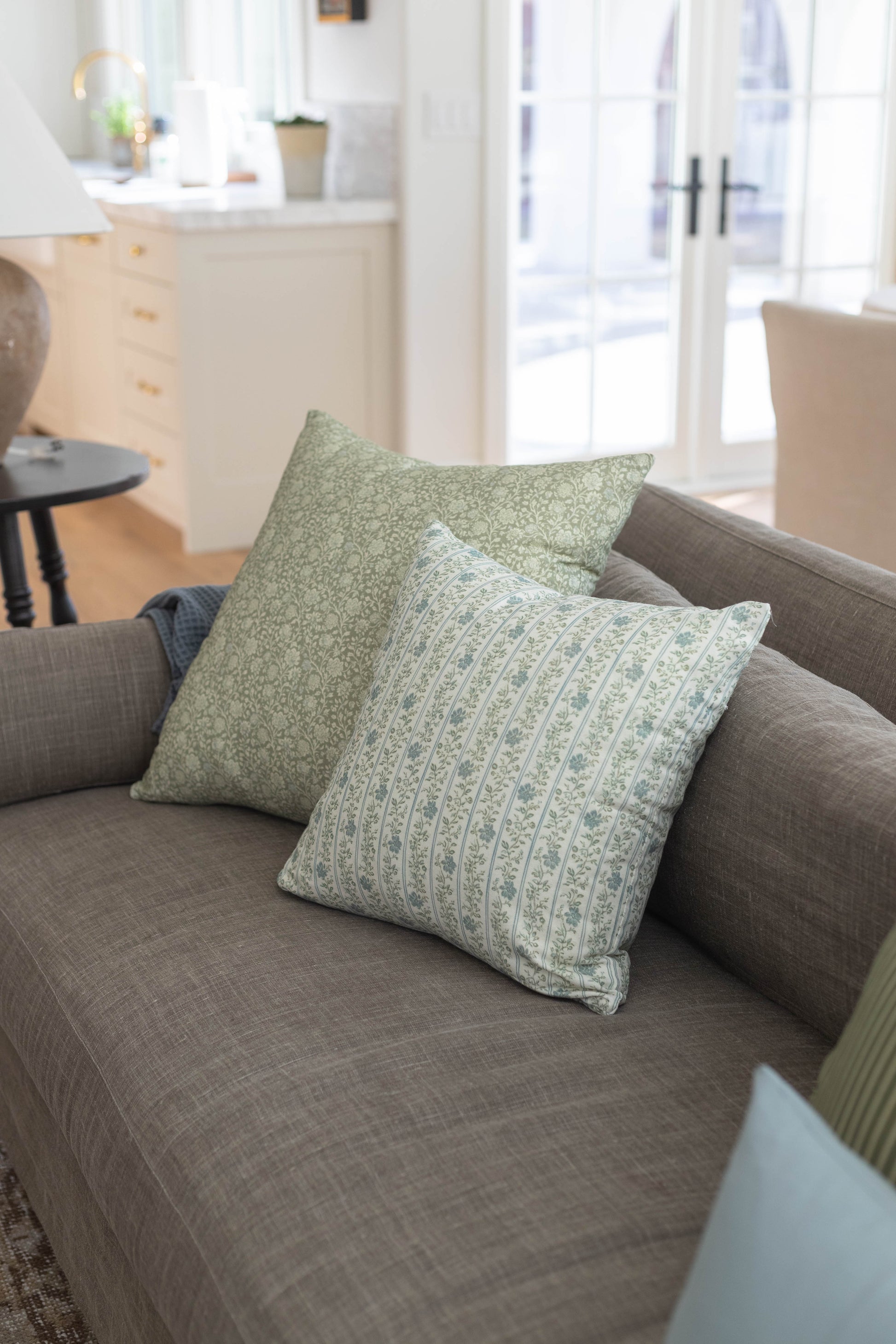 Green and cream patterned throw pillows arranged on a gray upholstered sofa in a bright living room.