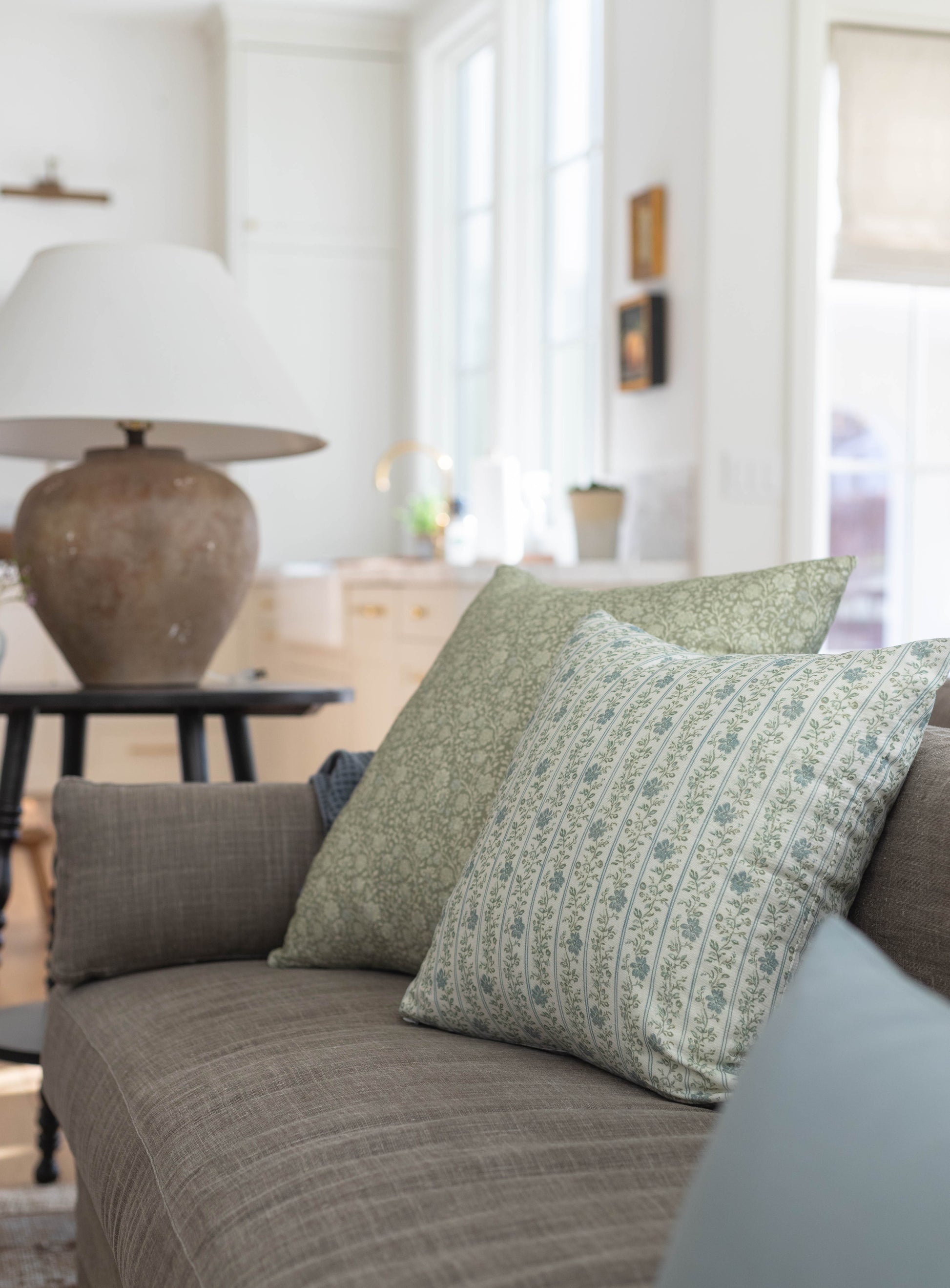 Green and cream patterned throw pillow with striped design on gray upholstered sofa.