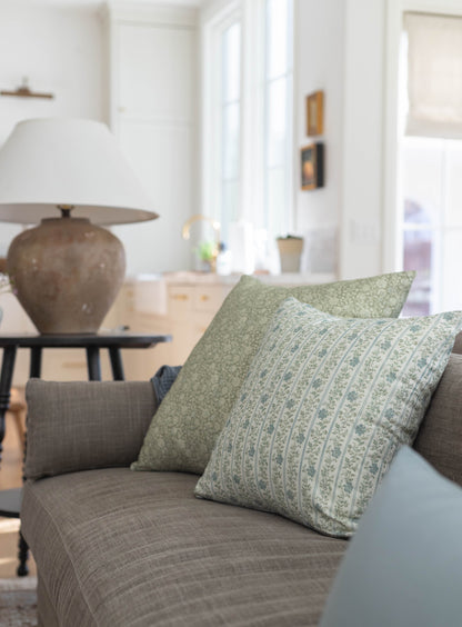 Green and cream patterned throw pillow with striped design on gray upholstered sofa.