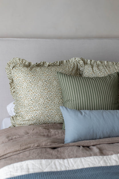 Green and cream patterned pillow with ruffled edges displayed on a bed with striped and solid pillows.