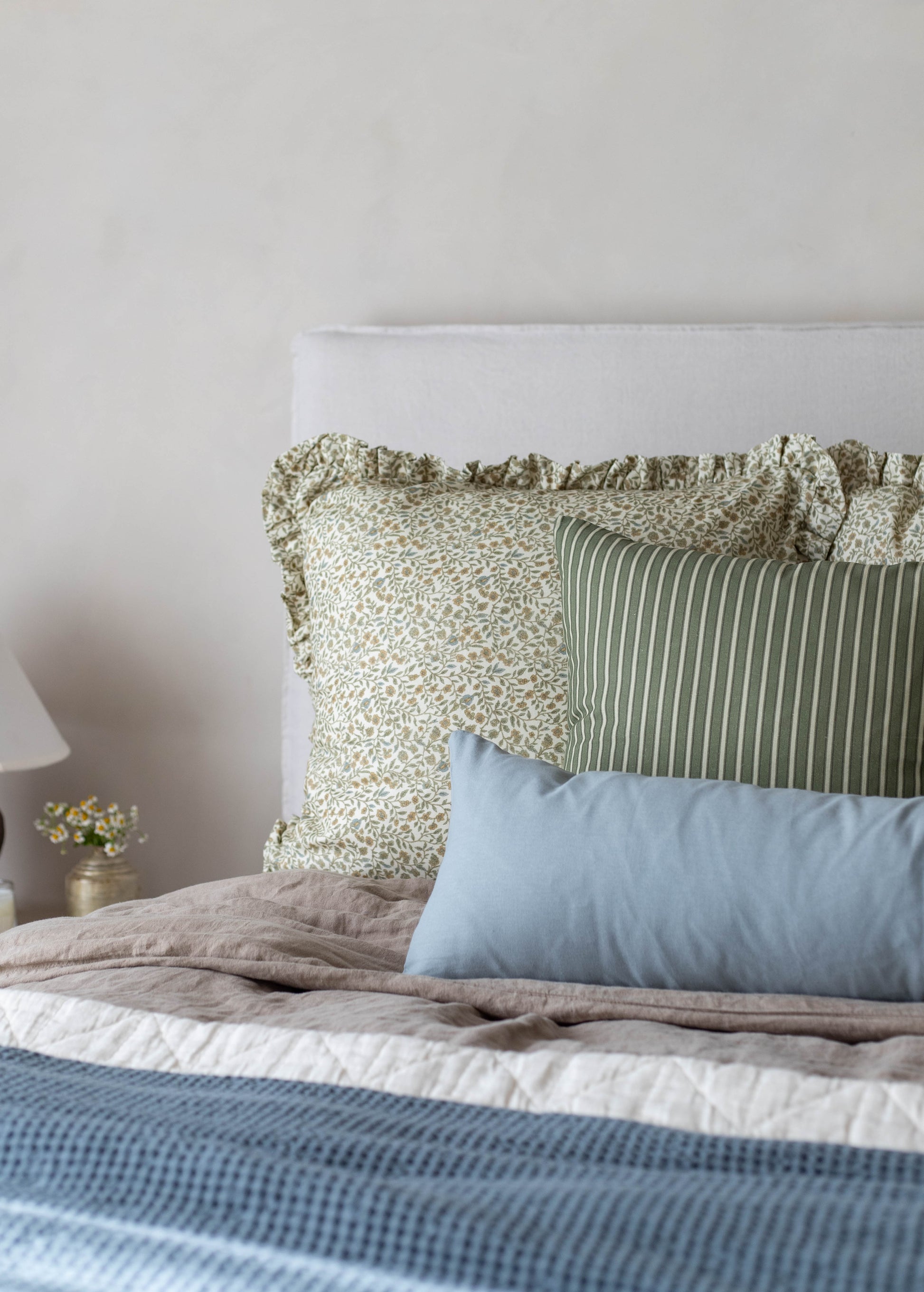 White upholstered headboard with green and cream patterned pillows and blue rectangular pillow arrangement on bed.