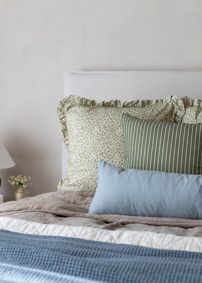 White upholstered headboard with green and cream patterned pillows and blue rectangular pillow arrangement on bed.
