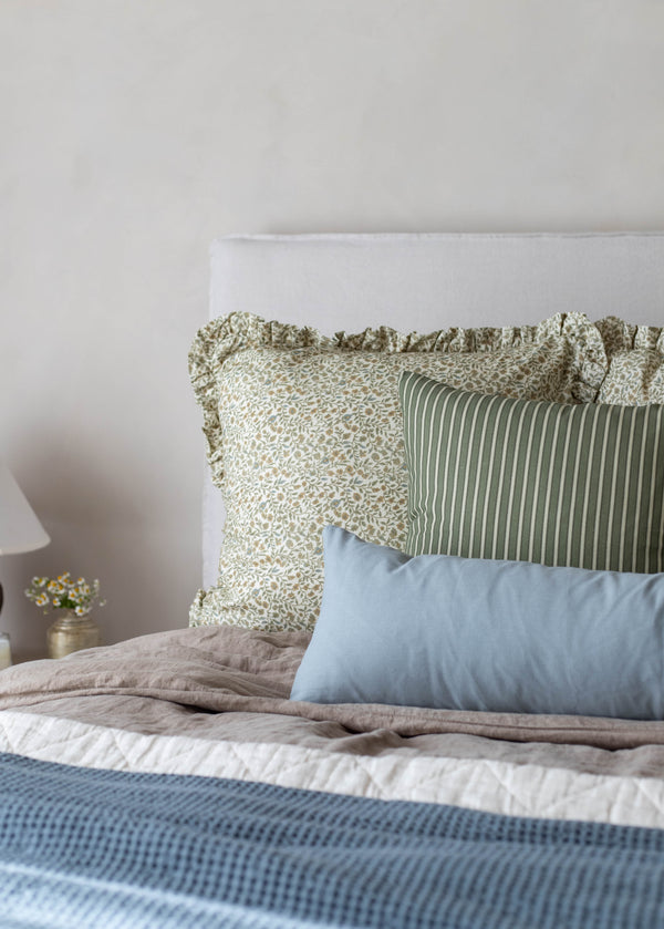 White upholstered headboard with green and cream patterned pillows and blue rectangular pillow arrangement on bed.