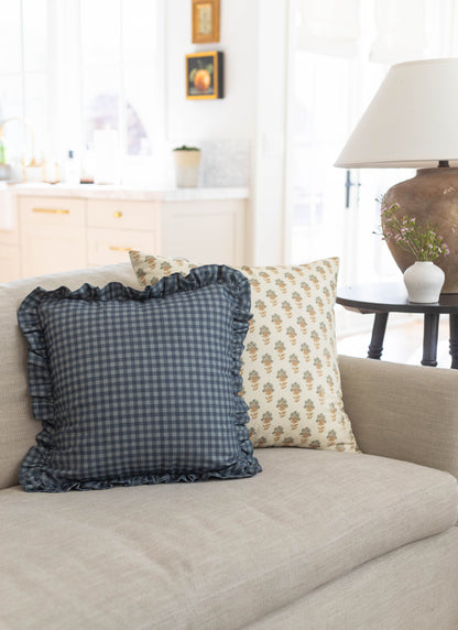 Blue gingham pillow with ruffled edges and cream floral pillow on beige sofa.