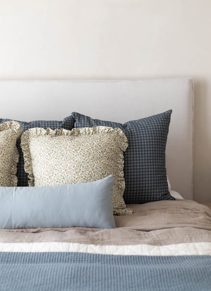 Navy gingham patterned pillow displayed on a bed with other decorative pillows and bedding.